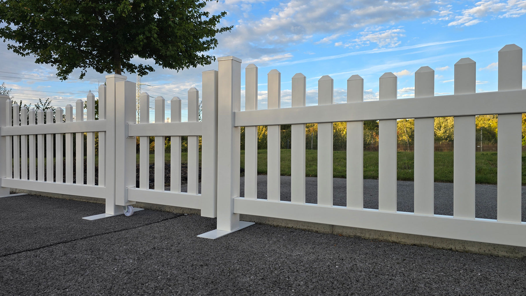 Side view of Simple Fencing portable scalloped picket fence panels in white with a central 3x3ft gate, highlighting the clean finish, with trees and sky in the background.