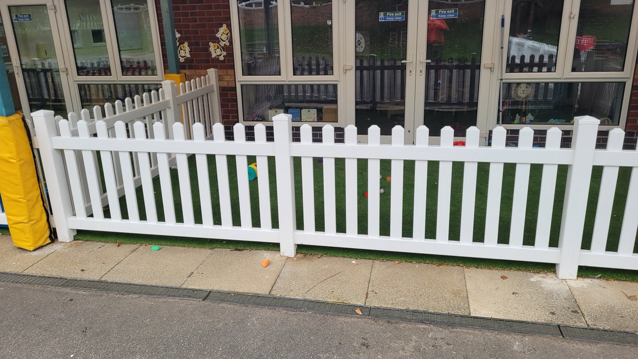 White PVC picket fence around an outdoor play area with artificial grass