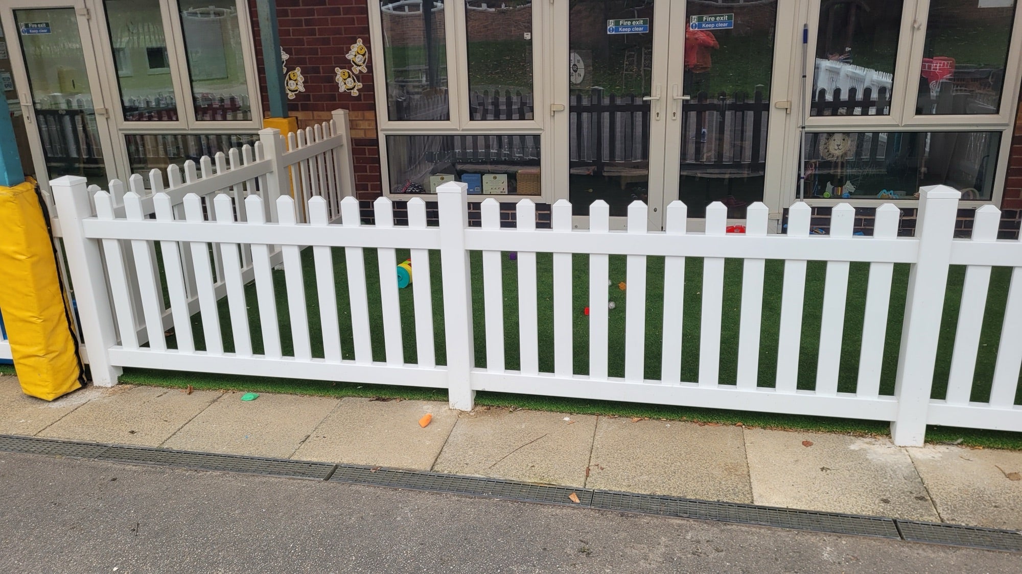 White PVC picket fence around an outdoor play area with artificial grass