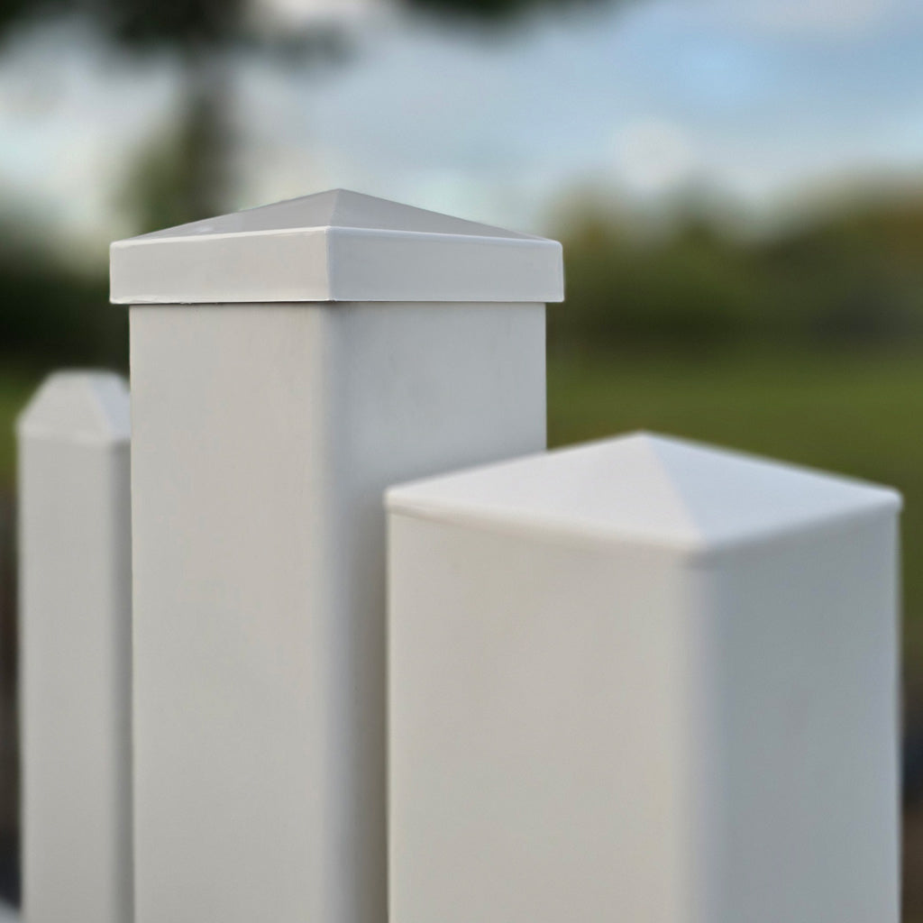 A close-up of white vinyl picket fence posts with New England post caps, showing the zero-maintenance finish, by Simple Fencing.