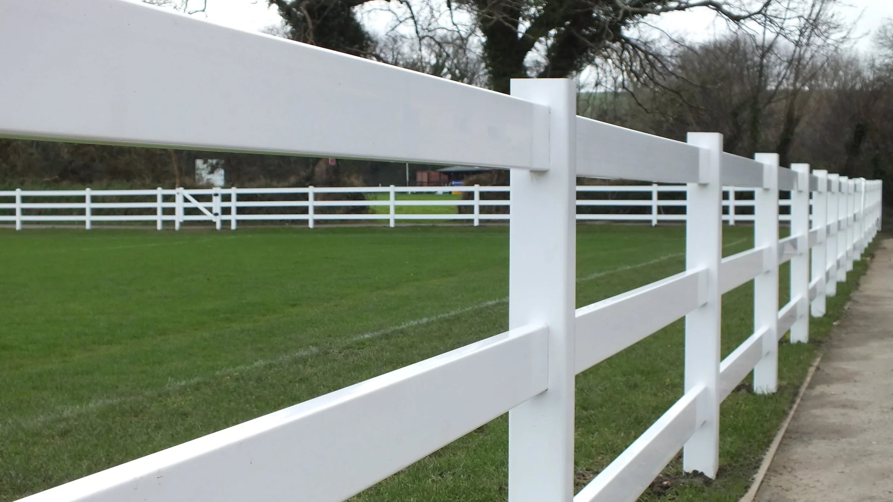 Simple Fencing white ranch 3-rail vinyl fence bordering a green cricket field.