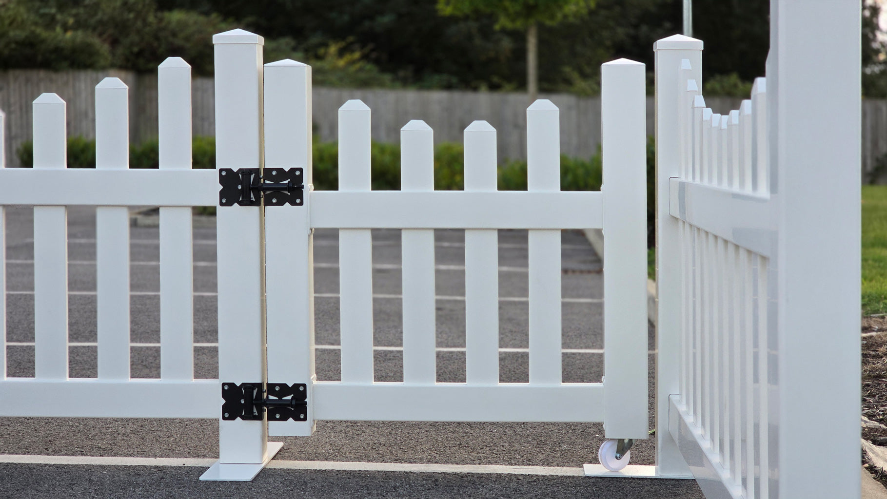 Classic scalloped picket gate, in white vinyl with black hardware, shown closed from a front perspective in a residential area.