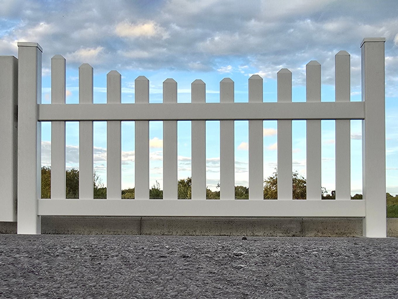 White picket fence with a blue sky and clouds in the background