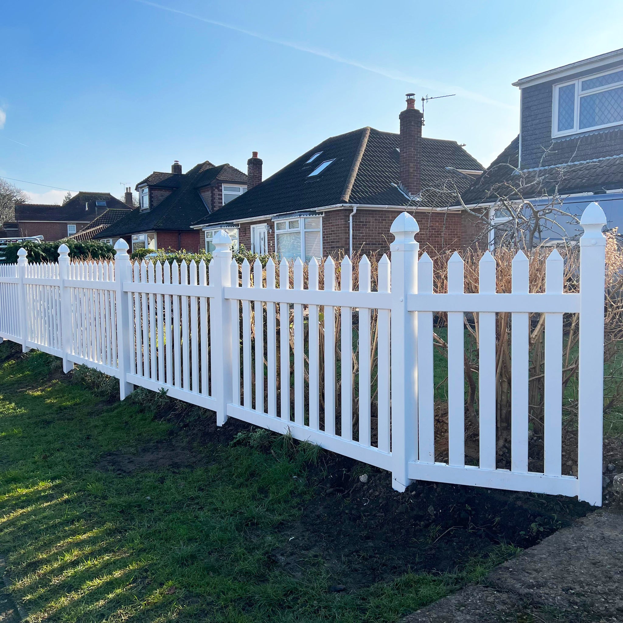 White picket fence in front of a residential house with clear blue sky by Simple Fencing.