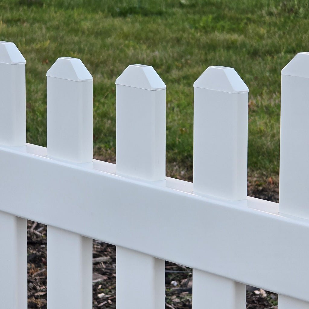 Close-up of a white picket fence with dog ear caps with grass in the background